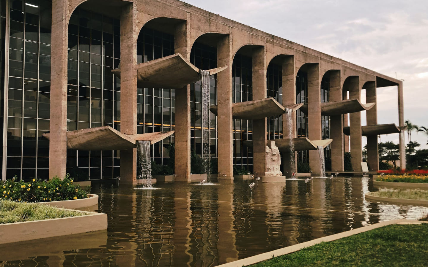 A modernist institutional building with a colonnade and reflecting pool