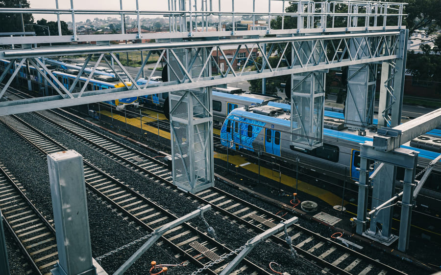 A passenger train at a rail station under overhead gantries